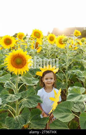 Petite fille souriante debout dans la prairie de tournesol en fleurs dans la campagne et regardant loin tout en tenant le tournesol et profiter de l'été Banque D'Images