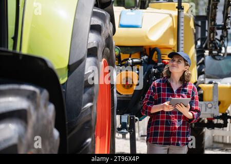 Agricultrice avec une tablette numérique à côté du tracteur agricole. Banque D'Images