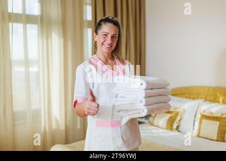 Portrait d'une belle femme de chambre d'hôtel tenant des serviettes propres et propres et montrant le pouce vers le haut. Banque D'Images