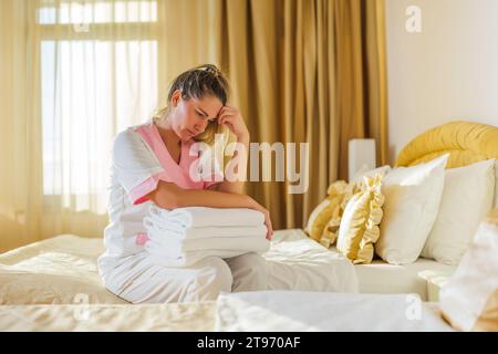 Image d'une femme de chambre triste surmenée assise sur le lit dans une chambre. Banque D'Images