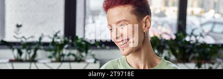 individu non binaire élégant et joyeux avec les cheveux courts riant au bureau, bannière horizontale Banque D'Images