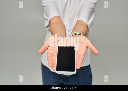 vue recadrée de la personne tenant le téléphone mobile avec écran vide sur fond gris, smartphone dans les mains Banque D'Images