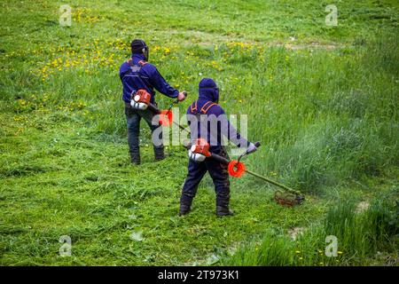 deux hommes de tondeuse municipale avec des coupe-bordures à fil coupant l'herbe à la journée ensoleillée Banque D'Images