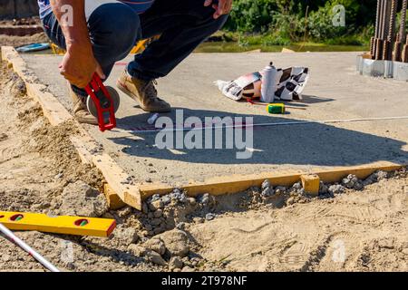 Le travailleur en position accroupie utilise un ruban de mesure de terrain pour mesurer avec précision la distance sur la dalle de béton du pont en construction. Banque D'Images