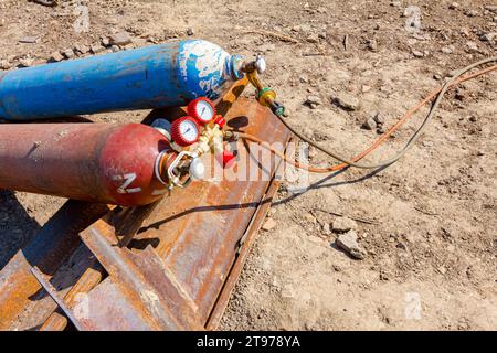 Équipements de soudage rouge et bleu, réservoirs d'oxygène et d'azote avec vannes et manomètres, bouteilles de gaz d'acétylène placées sur des pieux métalliques à la construction Banque D'Images