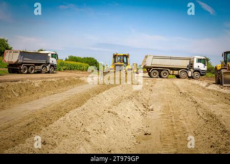 Les engins de terrassement caterpillar déplacent la terre sur le chantier de construction de tombereaux stationnés et un autre bulldozer est en arrière-plan. Banque D'Images