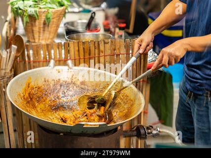 Chef cuisinant des fruits de mer sautés en pâte de curry jaune sur une poêle dans la nourriture de rue. Banque D'Images