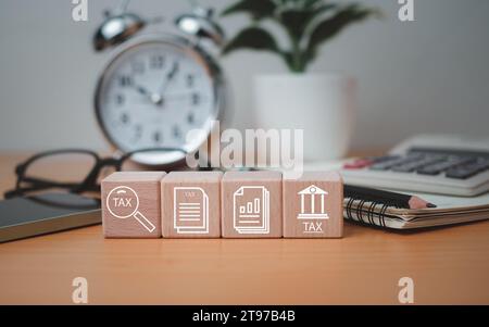 Icônes de symboles fiscaux imprimés en bloc de bois placées sur un plateau en bois avec des fournitures de bureau, des recherches financières, des rapports, des calculs de déclaration de revenus. Banque D'Images