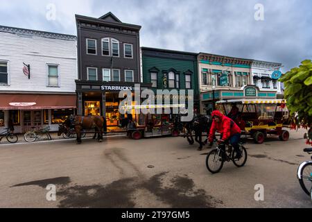 Les bâtiments de la rue principale rappellent une ville occidentale. Il y a des restaurants, des cafés, des magasins de souvenirs et des magasins de fudge. Il y a des calèches, des vélos et des piétons dans la rue. Scène de rue sur l'île Mackinac, où les véhicules à moteur sont interdits. Mackinac Island, Michigan, États-Unis Banque D'Images