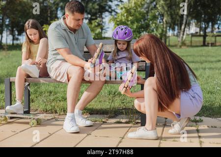 Les parents mettent des patins à roulettes sur leur fille au parc Banque D'Images