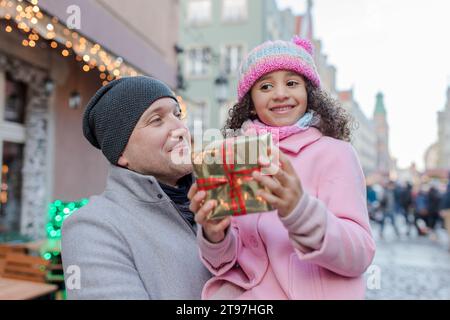 Père souriant avec sa fille tenant le cadeau au marché de Noël Banque D'Images