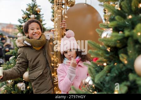 Heureux frère et sœur appréciant près des arbres de Noël au marché Banque D'Images