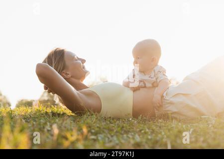 Mère heureuse couchée sur l'herbe avec son fils dans le parc au coucher du soleil Banque D'Images