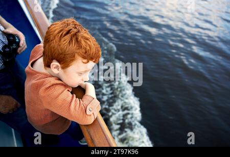 Redhead garçon appuyé sur la rampe et regardant la mer Banque D'Images