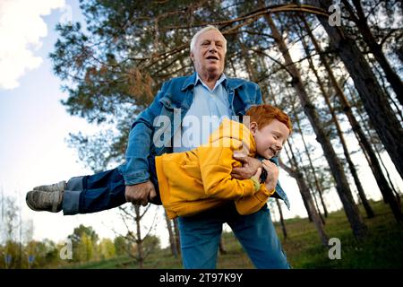 Homme aîné portant petit-fils et jouant dans le parc Banque D'Images