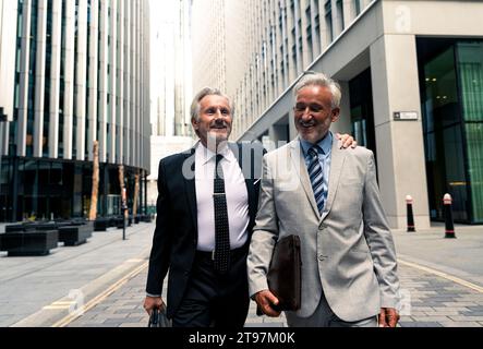 Heureux hommes d'affaires seniors marchant et parlant entre eux au milieu des bâtiments financiers Banque D'Images