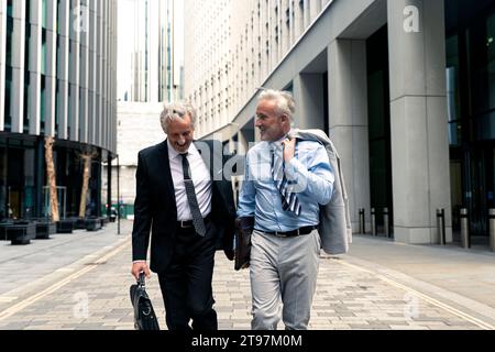 Souriant hommes d'affaires de haut niveau marchant et parlant les uns avec les autres Banque D'Images