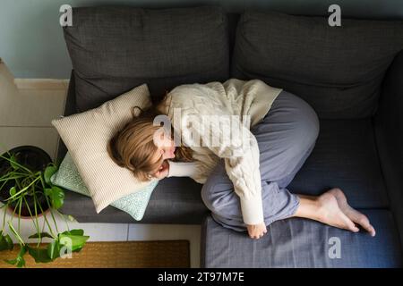 Femme avec maux d'estomac dormant sur le canapé à la maison Banque D'Images