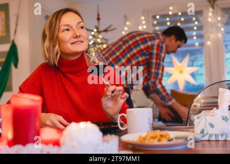 Femme blonde réfléchie ayant du vin rouge au dîner de Noël à la maison Banque D'Images