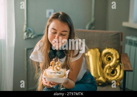 Femme souriante regardant le gâteau avec le numéro 18 bougies à l'anniversaire Banque D'Images