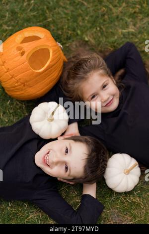 Garçon et fille couchés sur l'herbe près des citrouilles à Halloween Banque D'Images