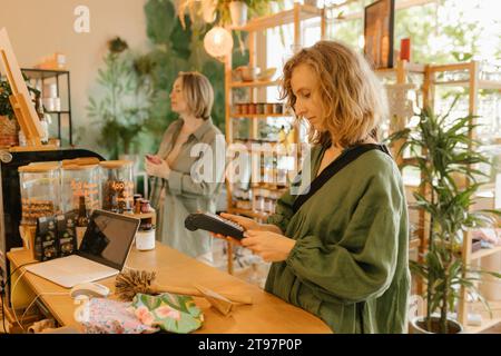 Femme blonde payant par lecteur de carte de crédit dans le café Banque D'Images