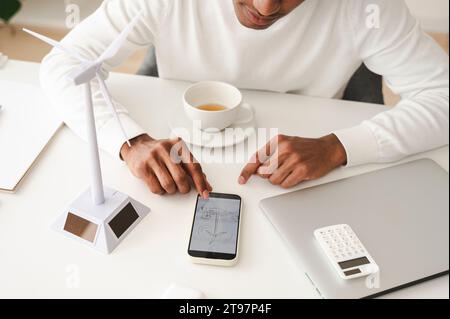 Homme d'affaires examinant le diagramme de turbine de vent sur le téléphone intelligent au bureau dans le bureau à domicile Banque D'Images