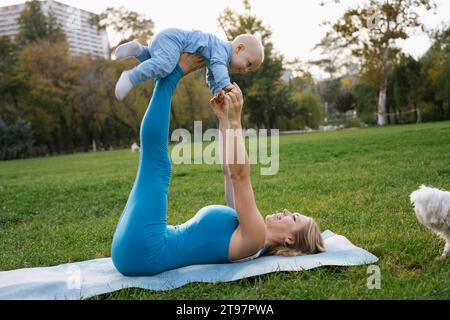 Mère et fils ludiques faisant du yoga près du chien dans le parc Banque D'Images