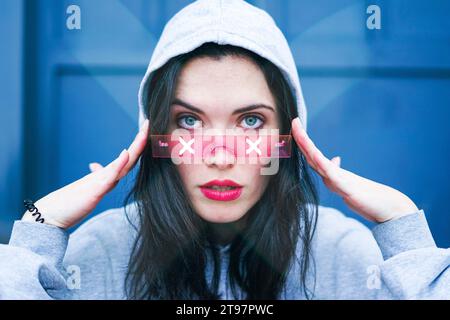 Jeune femme portant une chemise à capuche et ajustant des lunettes intelligentes Banque D'Images
