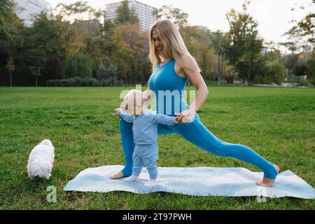 Mère souriante et fils faisant du yoga avec chien dans le parc Banque D'Images