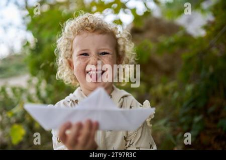 Fille heureuse sortant de la langue et tenant le bateau en papier Banque D'Images
