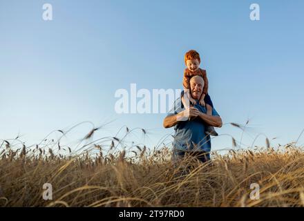 Grand-père souriant portant son petit-fils sur les épaules dans le champ de blé Banque D'Images