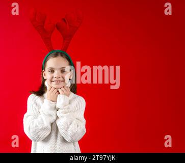 Enfant dans le bandeau de bois de renne souriant et regardant la caméra sur fond rouge Banque D'Images