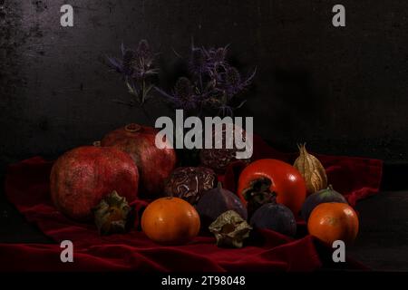 Divers fruits tropicaux et un chardon forment une nature morte sur un tissu de velours rouge foncé. Banque D'Images