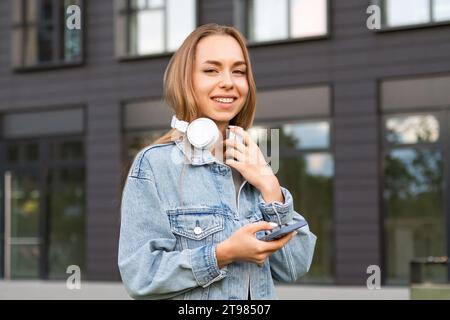 Une jeune femme avec une expression de contenu équilibre des écouteurs sur son cou tout en tenant un téléphone Banque D'Images