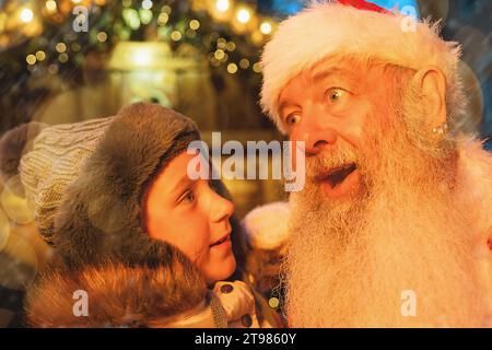 Enfant en admiration avec le Père Noël sur un marché de Noël, entouré de lumières festives Banque D'Images