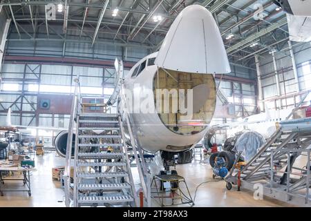 Vue de face de l'avion de passagers blanc en maintenance dans le hangar de l'aviation. L'avion a ouvert un radar météorologique. Vérification du système mécanique Banque D'Images