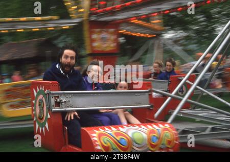 1980s, une famille, maman, papa et jeune fille assis ensemble enjolihg un tour d'amusement palpitant à un parc d'expositions... le père avec un visage de terreur... est-il vraiment effrayé?? Banque D'Images