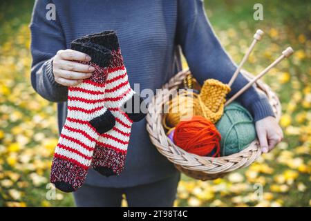 Tricot et crochet hobby. Femme tenant à la main paire de chaussettes tricotées et boules colorées de laine dans le panier Banque D'Images