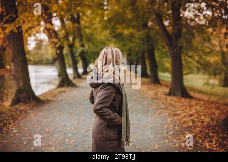 Femme élégante avec trench-coat brun et écharpe est debout dans l'allée au parc d'automne. Beauté et mode de vie Banque D'Images