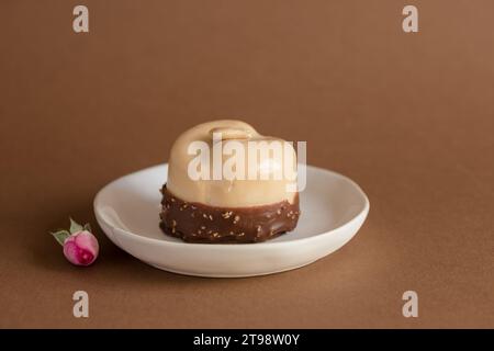 Mini tarte avec mousse de chocolat blanc et amande sur le dessus, avec rose rose et grains de café à côté, servi sur assiette blanche, isolé sur fond brun Banque D'Images