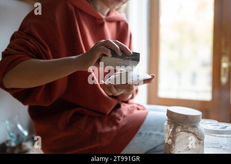 Les mains de céramiste féminine nettoient la surface de la soucoupe stockée longtemps dans des conditions inappropriées à la maison Banque D'Images