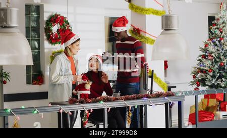 Le directeur du bureau décoré de Noël délègue des tâches aux travailleurs avant la saison des vacances d'hiver. Superviseur expliquant aux employés comment terminer correctement le projet dans l'espace de travail Noël orné Banque D'Images