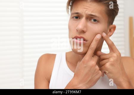 Bouleversé jeune homme qui fait sauter un bouton sur son visage à l'intérieur. Problème d'acné Banque D'Images