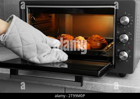 Femme sortant du moule à pâtisserie avec de délicieux petits pains en spirale du four électrique, closeup Banque D'Images