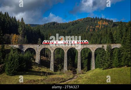 Telgart, Slovaquie - le célèbre viaduc de Chmarossky dans les basses Tatras par une journée d'automne ensoleillée avec un ciel bleu et des nuages. Un train régulier passe par le Banque D'Images