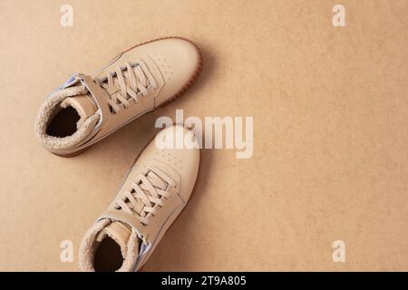 Baskets unisexes en cuir beige avec lacets et semelles en caoutchouc sur fond beige. Vue de dessus de la pose plate. Chaussures de sport décontractées. Banque D'Images