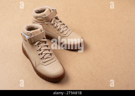 Baskets unisexes en cuir beige avec lacets et semelles en caoutchouc sur fond beige. Vue de dessus de la pose plate. Chaussures de sport décontractées. Banque D'Images