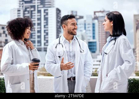 Heureux, les médecins et parler de soins de santé sur la pause-café, en plein air et se détendre à l'hôpital, la clinique ou des collègues sur le toit. Chirurgien, sourire et profiter Banque D'Images