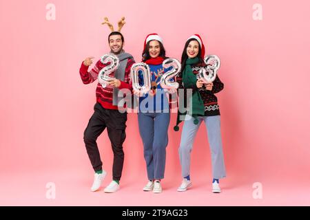 Studio photographié portrait en longueur Noël 2023, groupe d'amis heureux masculins et féminins portant des chandails sur fond rose isolé Banque D'Images